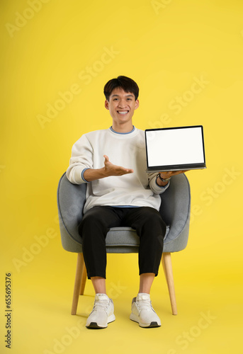 full body of young Asian man wearing sweater and using latop on yellow background