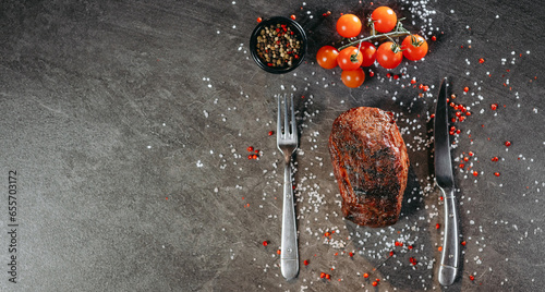 Tableau sur toile A generous piece of grilled steak on a table with fork and knife cutlery and gre