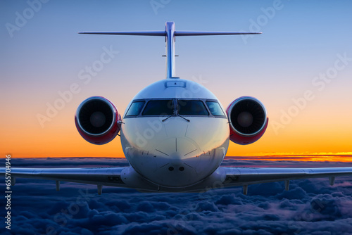 Front view of the executive airplane flies in the sunset sky