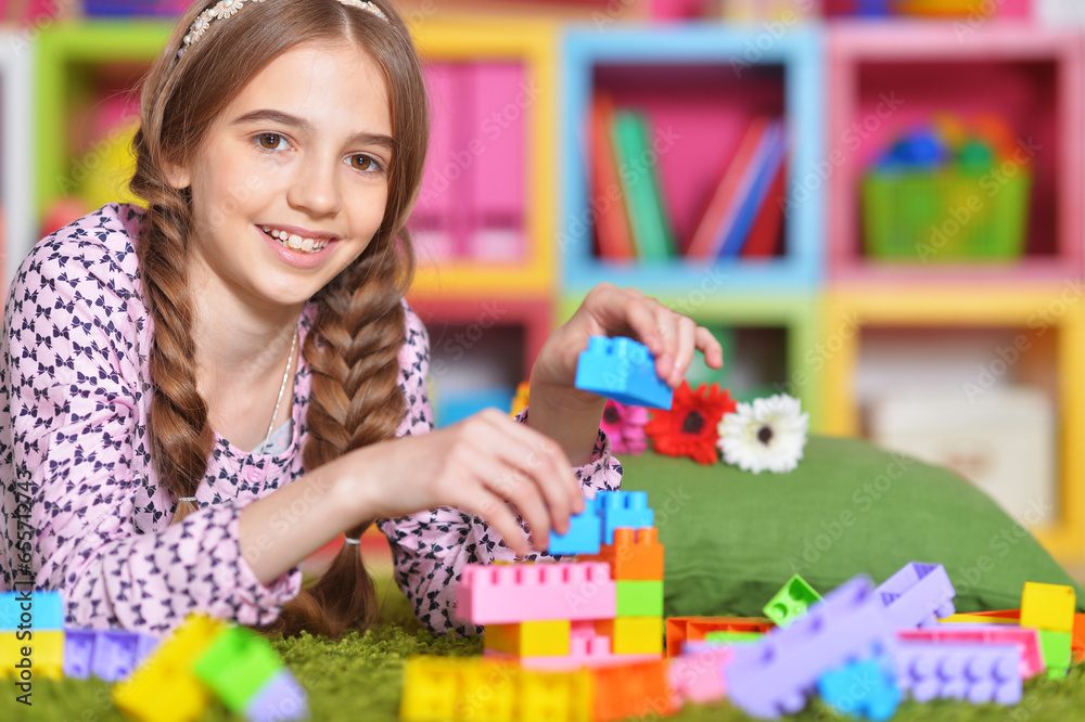Fototapeta premium Portrait of cute girl playing with colorful plastic blocks in room