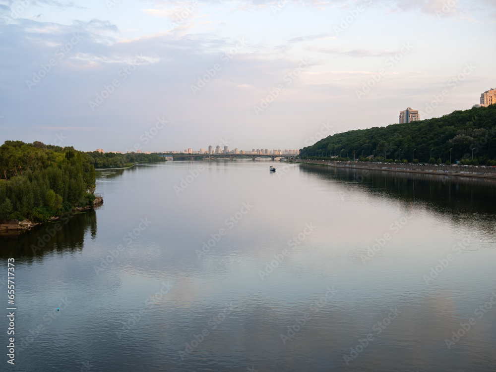 View of the Metro Bridge over the Dnipro River, a floating ship and tall buildings in the distance in Kyiv