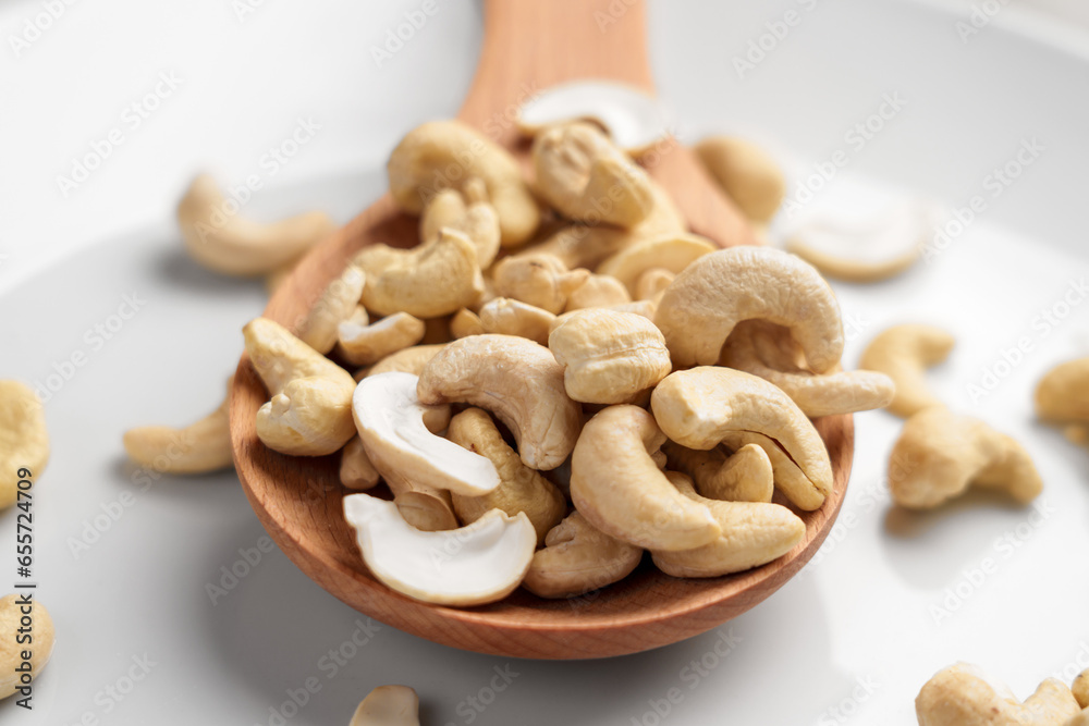 Raw nourishing cashew in kitchen wooden spoon on white ceramic surface Raw nourishing cashew in kitchen wooden spoon on white ceramic surface
