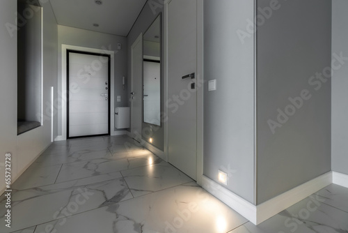 White entrance door inside the apartment in a modern interior. LED backlighting in the wall