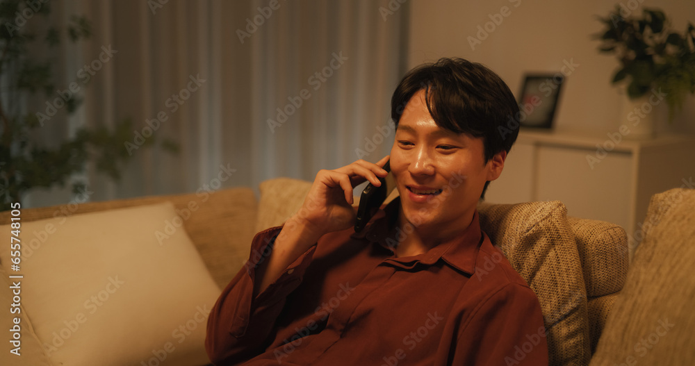 Young South Korean Man is Relieved to Get Positive News on a Phone. Happy Asian Male Smiles While Having a Conversation on a Call with a Friend. Handsome Man Resting on Couch at Home Before Sleep Young South Korean Man is Relieved to Get Positive News on a Phone. Happy Asian Male Smiles While Having a Conversation on a Call with a Friend. Handsome Man Resting on Couch at Home Before Sleep