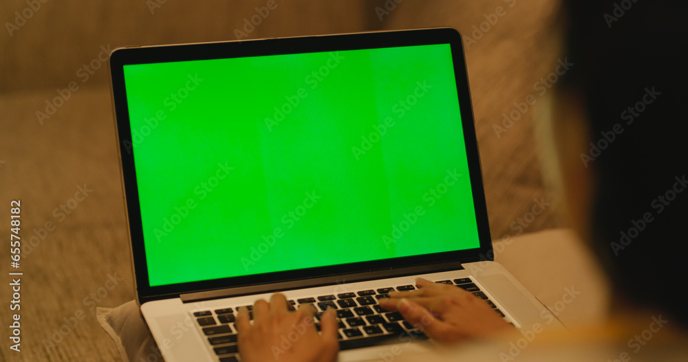 Over the Shoulder Shot of an Unidentified Woman Busy with Office Work, Using a Laptop Computer with Green Screen Mock Up Display for Remote Work in Her Cozy Home Workspace on a Couch Over the Shoulder Shot of an Unidentified Woman Busy with Office Work, Using a Laptop Computer with Green Screen Mock Up Display for Remote Work in Her Cozy Home Workspace on a Couch