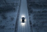 aerial view of a black vehicle driving on a rural winter road with headlights shining. bird's eye view of an SUV on snowy icy landscape. Generative AI