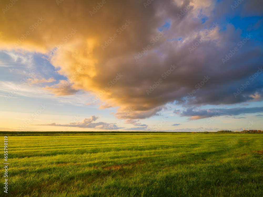 Natural landscape during sunset. Huge yellow clouds and blue sky. Field and meadow. Huge cloud in the sky after a storm. Natural landscape. Wallpaper and background.