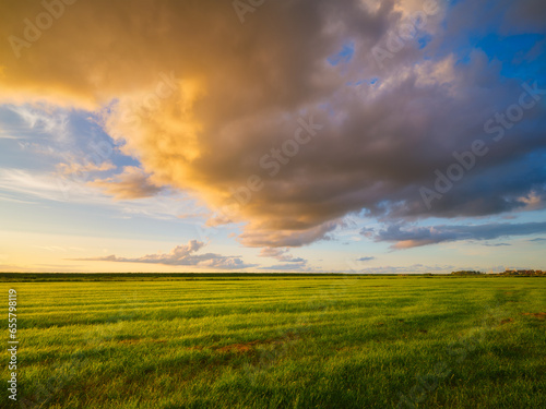 Natural landscape during sunset. Huge yellow clouds and blue sky. Field and meadow. Huge cloud in the sky after a storm. Natural landscape. Wallpaper and background.