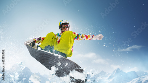 Sportive girl in uniform and helmet riding snowboard over snowy mountain and blue sky background on sunny day. Concept of winter sport, action, motion, hobby, leisure time. Banner. Copy space for ad