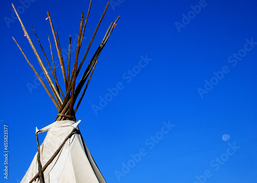 Top of a Native American tip or wigwam stands against a bright, blue sky.