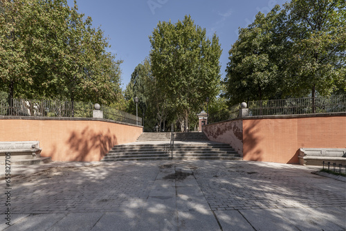 Stone stairs between red brick walls at the access to an urban park with lots of leafy trees