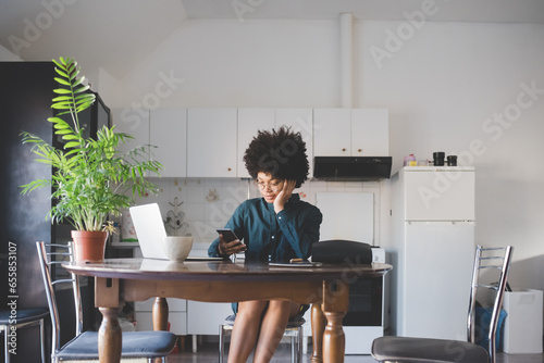 Young multiethnic woman indoors at home using computer and smartphone