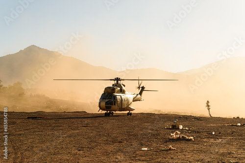 A military helicopter is seen flying and landing in desert at sunset in a cloud of dust. Air force aircraft photo