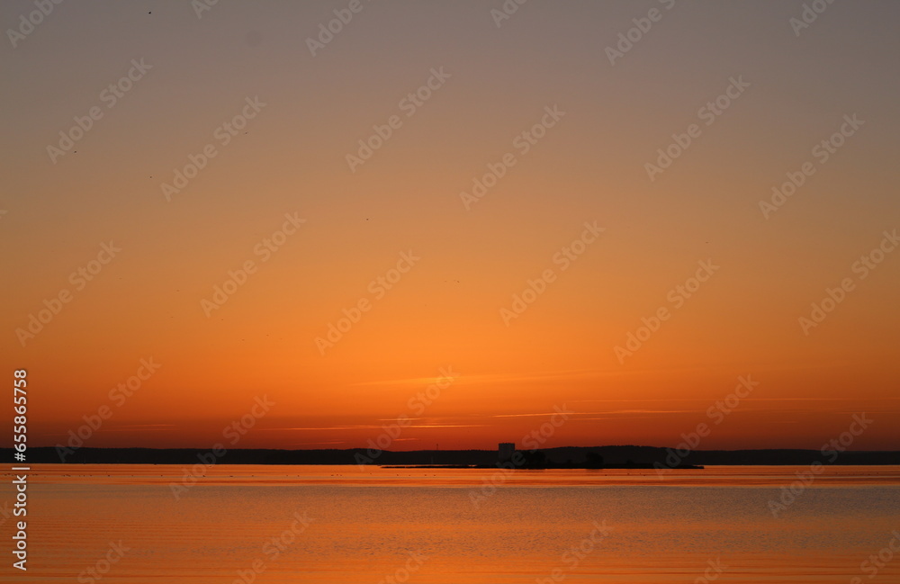 Orange sunset over the water. A beautiful fabulous horizon and the setting sun over the lake. Evening seascape.