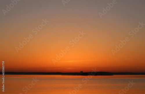 Orange sunset over the water. A beautiful fabulous horizon and the setting sun over the lake. Evening seascape.