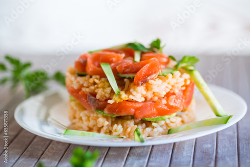 Boiled white rice with salted red fish, cucumbers and other vegetables with herbs in a plate.
