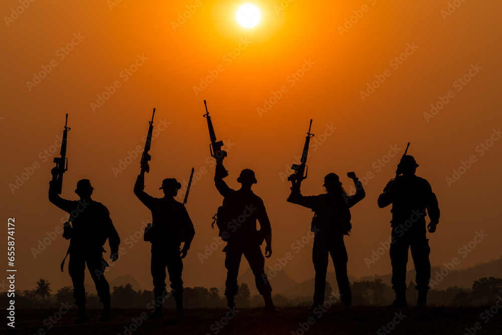 silhouette group of special forces sodiers standing and holding gun over the sunset and colorful orange sky background