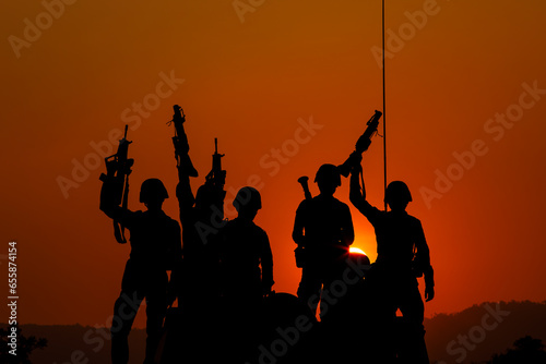 silhouette group of special forces sodiers standing and sit holding gun on cannon tank with over the sunset and colorful orange sky background,