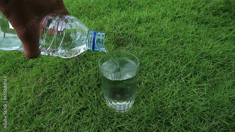 Pouring mineral water from a bottle into a glass. Pouring water into a glass on the grass. Pouring mineral water from a bottle into a glass. Pouring water into a glass on the grass.
