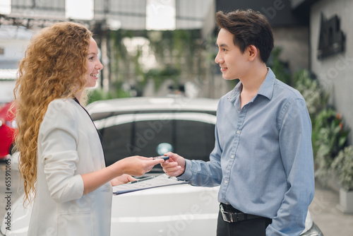 A beautiful female car sales employee gives the keys to the customer who has duly signed the purchase contract. Car rental  dealership successful sale of a car  purchase contract  and delivery of key.