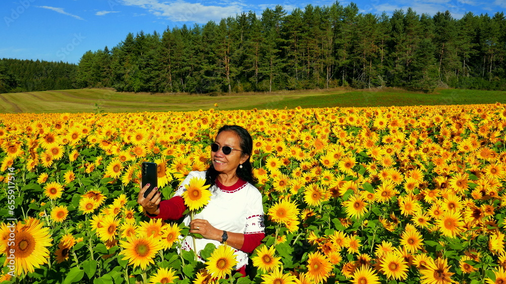 lächelnde Asiatin macht Selfie in einem großen blühendem Sonnenblumenfeld unter blauen Himmel lächelnde Asiatin macht Selfie in einem großen blühendem Sonnenblumenfeld unter blauen Himmel