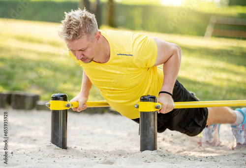 Man doing push ups with horizontal bar outdoors in park for healthy wellbeing. Sportsman guy making strong workout for muscle