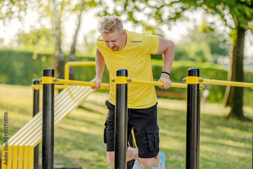 Man doing push ups with horizontal bar outdoors in park for healthy wellbeing and arm workout. Sportsman guy making strength training for muscle