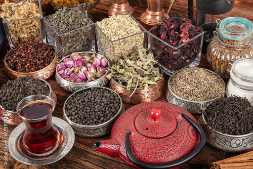 Set of different types of green, black and herbal teas next to a cast iron teapot filled with hot brewed tea on a wooden background. Delicious organic drinks. Look from above.
