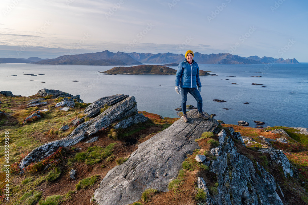 hiking woman on hill, autumnal nature of Norway. Hiking by the fjord and mountains on the island of Kvaløya in Troms, between orange and red colored plants and birch. place to relax, hikers paradis - obrazy, fototapety, plakaty 