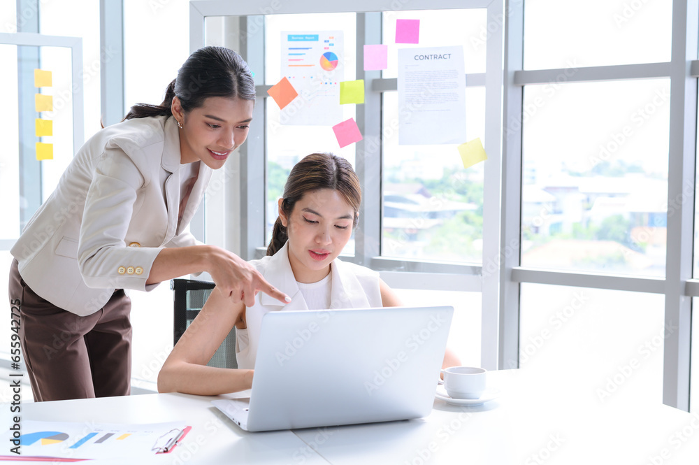 Attractive senior businesswoman train or mentor coach speaking to young woman. Two young Asian businesswomen working with laptop in the office. Attractive senior businesswoman train or mentor coach speaking to young woman. Two young Asian businesswomen working with laptop in the office.
