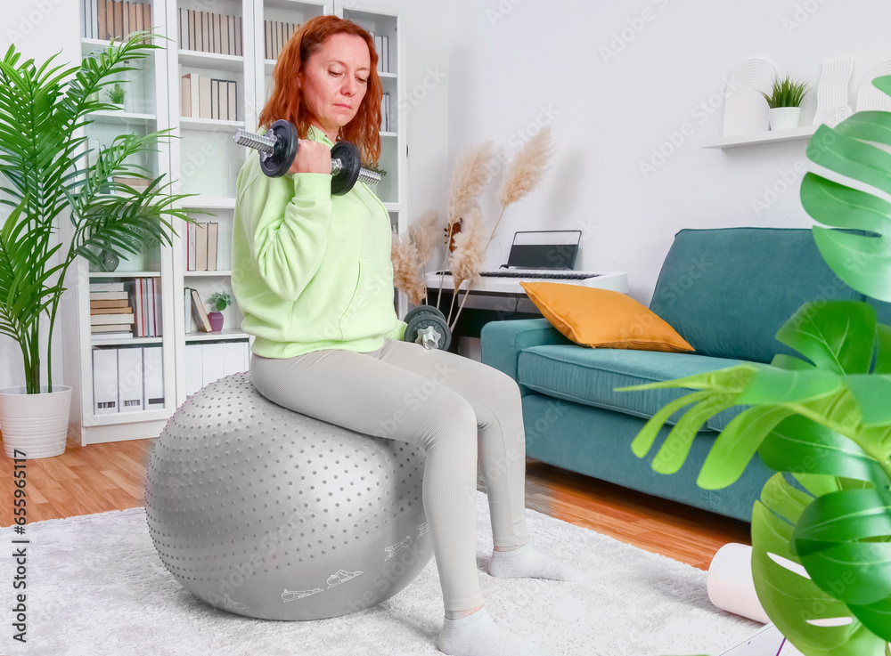 woman doing sports exercises with fitness ball and dumbbells at home