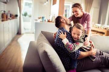 Happy young caucasian family being playful and having fun on the couch at home