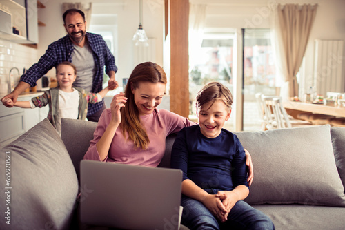 Happy young caucasian family being playful at home and using a laptop on the couch © Geber86
