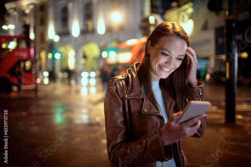 Happy young caucasian woman using a phone in the city at night