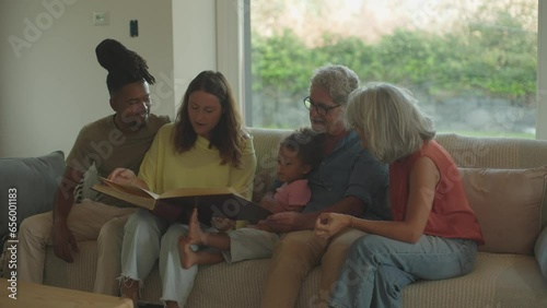 relations in multi-ethnic family : daughter and her young husband watching photo album with relatives photo