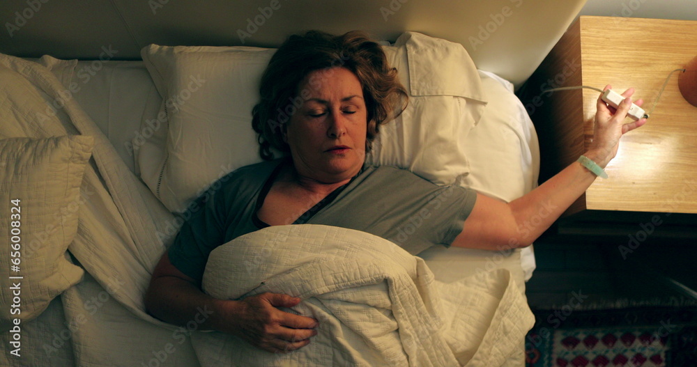 Woman lying in bed preparing to go to sleep, senior switching nightstand light OFF, person going to sleep