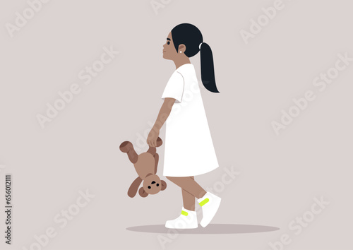 A baby girl in a white dress playfully holding a teddy bear upside down by its paw