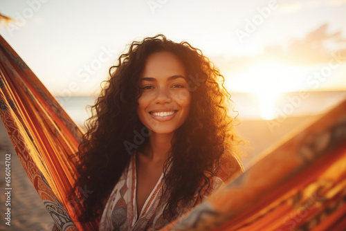 Mixed race woman on beach holiday lying in hammock reading book during sunset