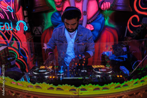 Young DJ of Indian origin playing Bollywood music in a room with special lights. Concept: music, fun, nightlife