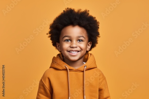 Studio Photography of a black 6 year Boy in an orange hoodie smiling at the Camera in front of an orange background Genertive Ai