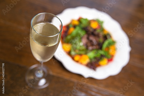 top view of a warm salad with mushrooms and herbs in a white plate with a glass of wine on the table