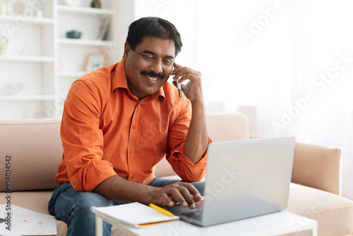 Indian businessman working from home, using laptop, have phone conversation