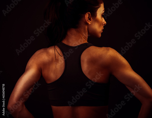 Serious female sporty muscular with ponytail doing stretching workout the shoulders, blades and arms in sport bra, standing on dark shadow grey background with empty copy space. Back view. Lifestyle © nastia1983