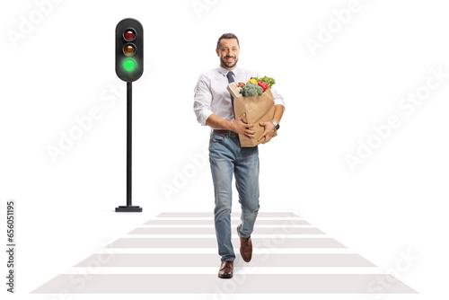 Full length portrait of a smiling professional man walking at a pedestrian and carrying a bag with fruits and vegetables