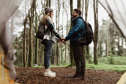 Happy young caucasian lady and man in jackets holding hands near tent, enjoy adventure, free time together