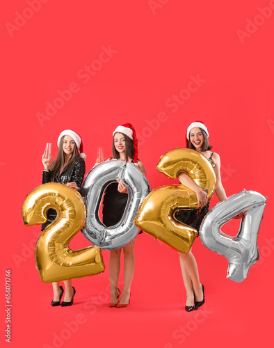Happy beautiful women with balloons in shape of figure 2024 and champagne glasses on red background