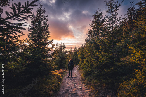 Young woman walking on a gravel path in forest, during sunset in czech mountains. Beautiful sky on spring.
