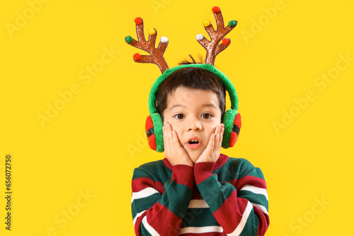 Surprised little boy in reindeer horns on yellow background