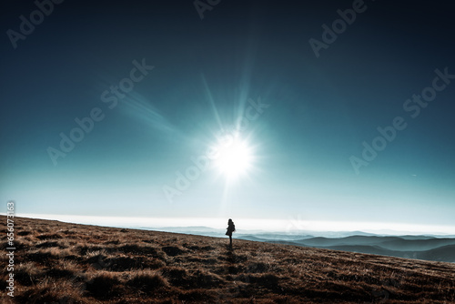 Woman stands on horizon hills with big shinning sun above her head, Krkonose, Czech republic, minimalistic nature scene, blue beautiful skies
