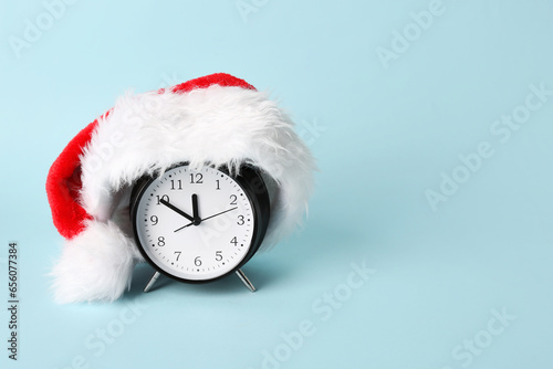 Alarm clock with Santa hat on blue background